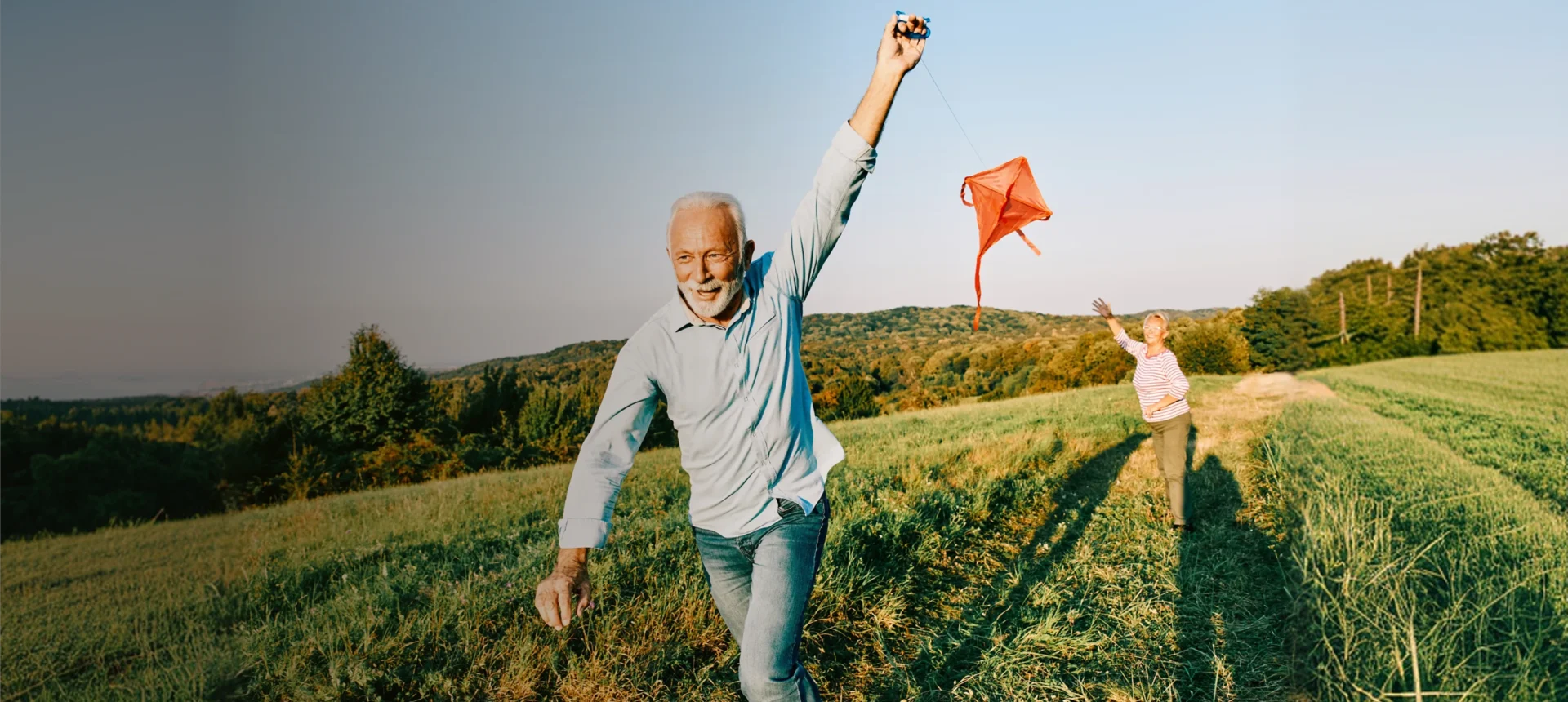 Older man joyfully flying a kite on a sunny day.