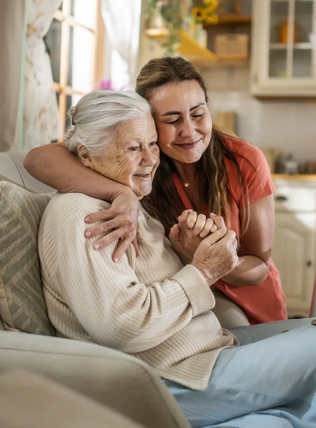 A young woman hugging an elderly woman affectionately at home.