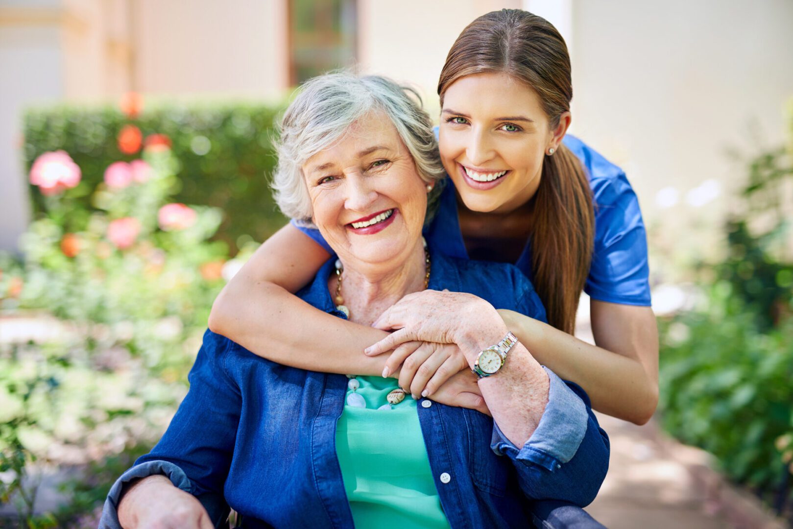 A young woman hugging an elderly woman outdoors, both smiling warmly.