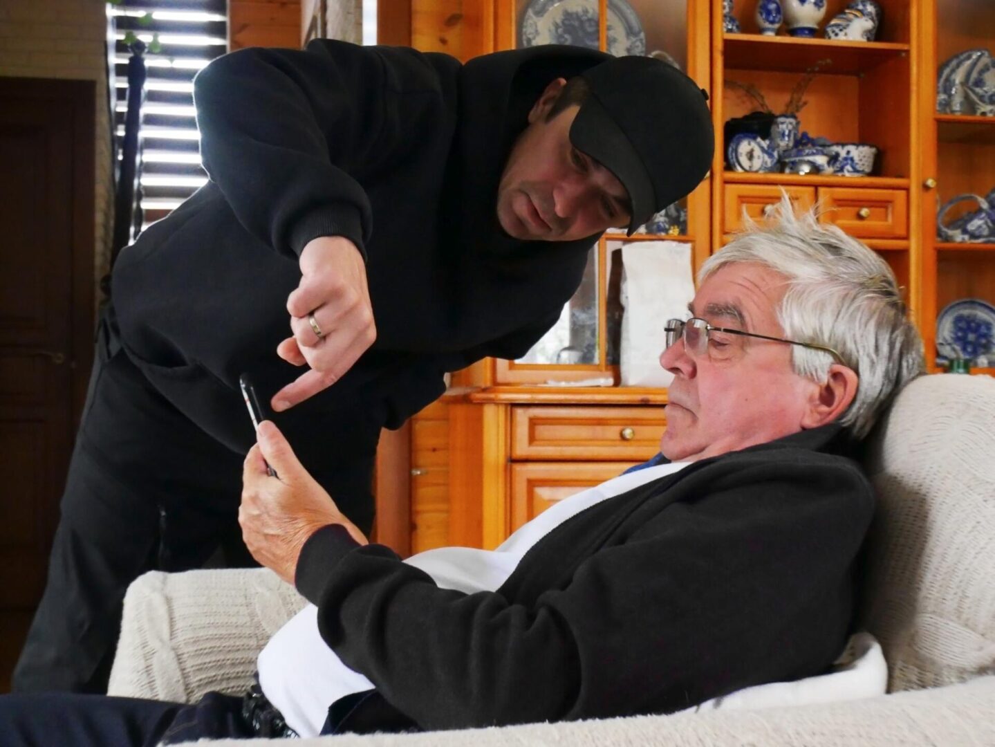 A young man showing a smartphone screen to an older man sitting on a couch.